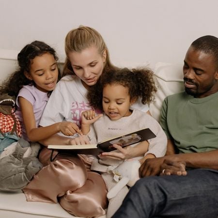 a mom and a dad reading a book to their two young daughters on the couch