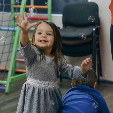 a young girl wearing a dress plays with bubbles in a classroom