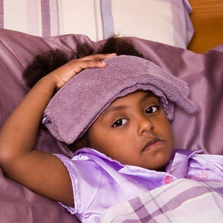 a young girl looks sadly at the camera wearing pajamas with a purple washcloth on her head