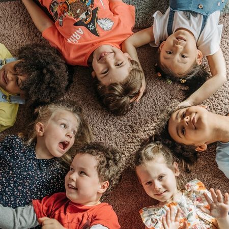 a group of 7 kids lay on a rug and smile at the camera