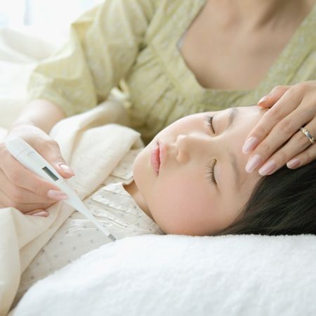 a mom takes her daughter's temperature while she lays down in bed