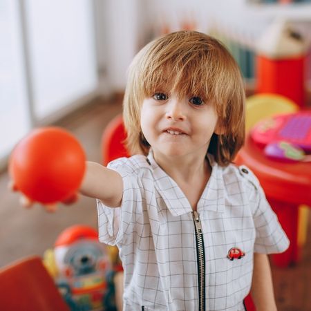 a young boy holds out a ball toward the camera and smiles
