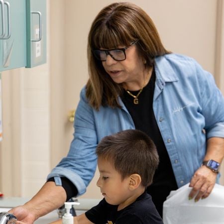teacher helping a young boy wash his hands