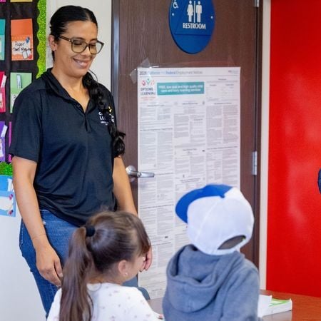 an Options for Learning stands and smiles at a young boy and young girl in a classroom near the bathroom
