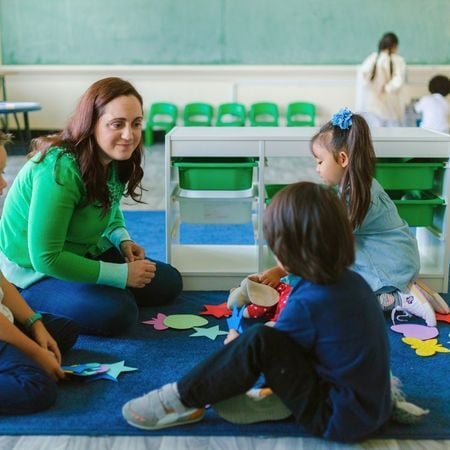 a teacher helps children play with different paper shapes on a rug
