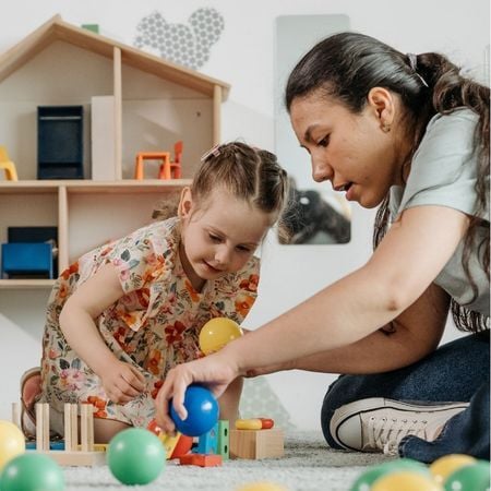 a teacher plays with blocks with a young girl in a classroom