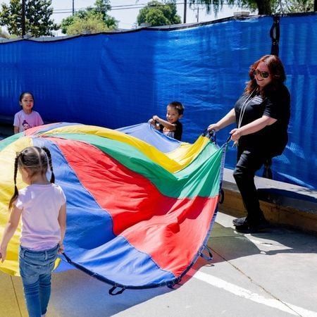 an Options for Learning teacher and a group of TK-age kids playing with a parachute outside