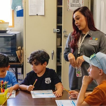 an Options for Learning teacher helps three boys complete a worksheet in class