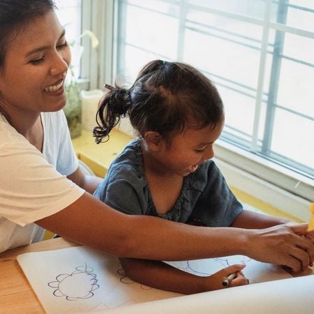 a mother helps her daughter draw on a canvas with crayons