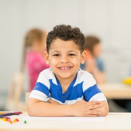 a young boy smiles at the camera with his arms crossed