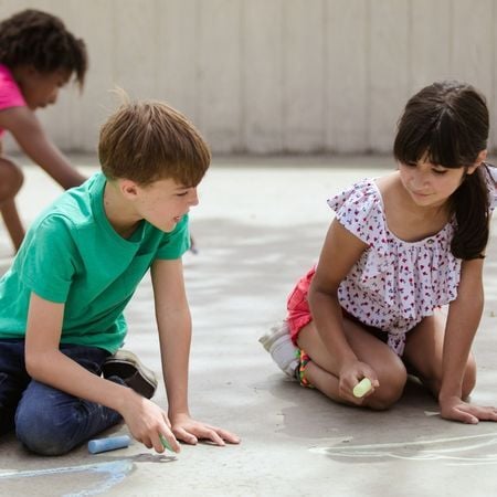 a young girl and boy draw on the pavement with chalk
