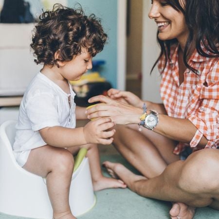 a mom watches her toddler as he sits on his toddler potty