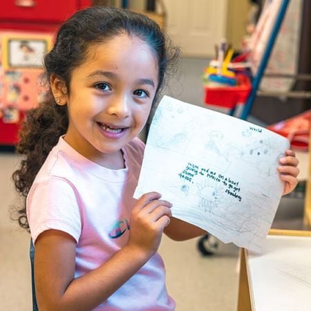 young girl holding up a drawing