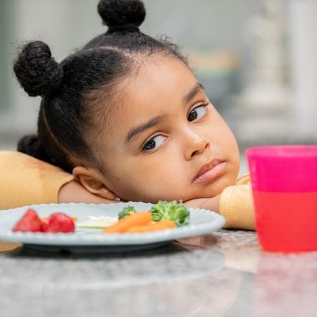a girl staring at a place of food with her hands on the table looking sad