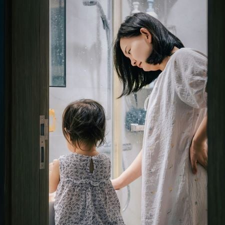 a mom watching her toddler-age daughter washing her hands in the bathroom