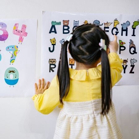 a young girl pointing to a visual poster of letters of the alphabet
