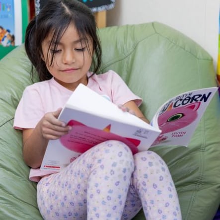 TK-age girl reading a book on a green beanbag