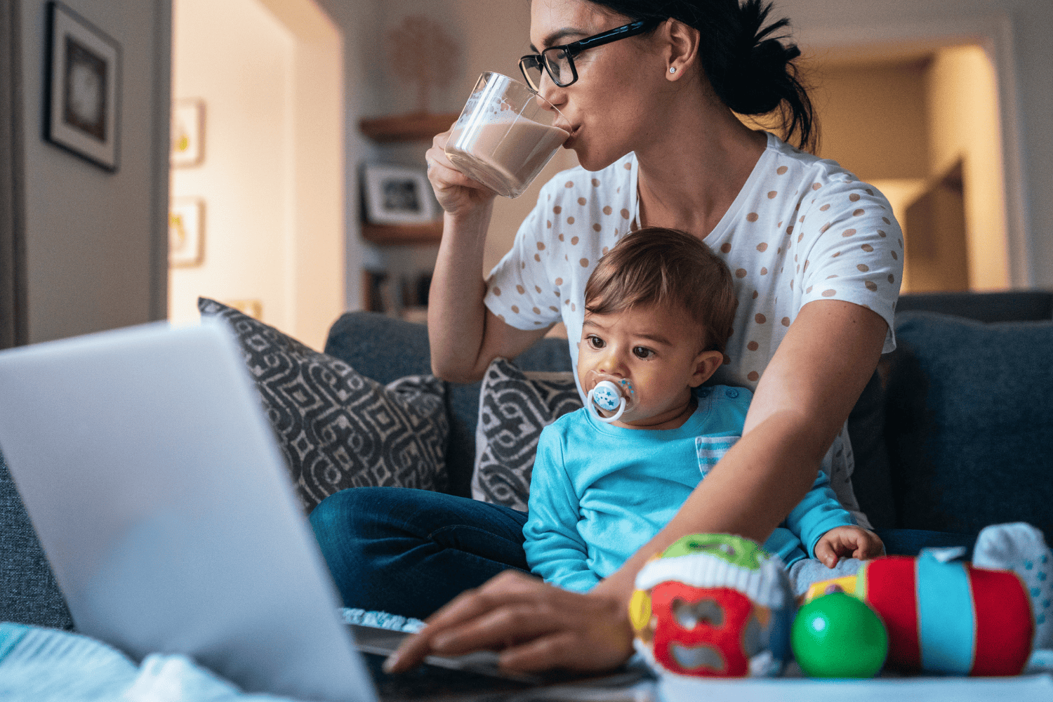 Mother holding young child while working on computer
