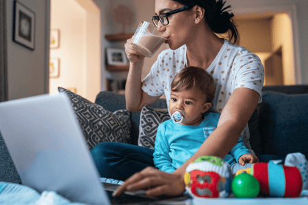 Mother holding young child while working on computer