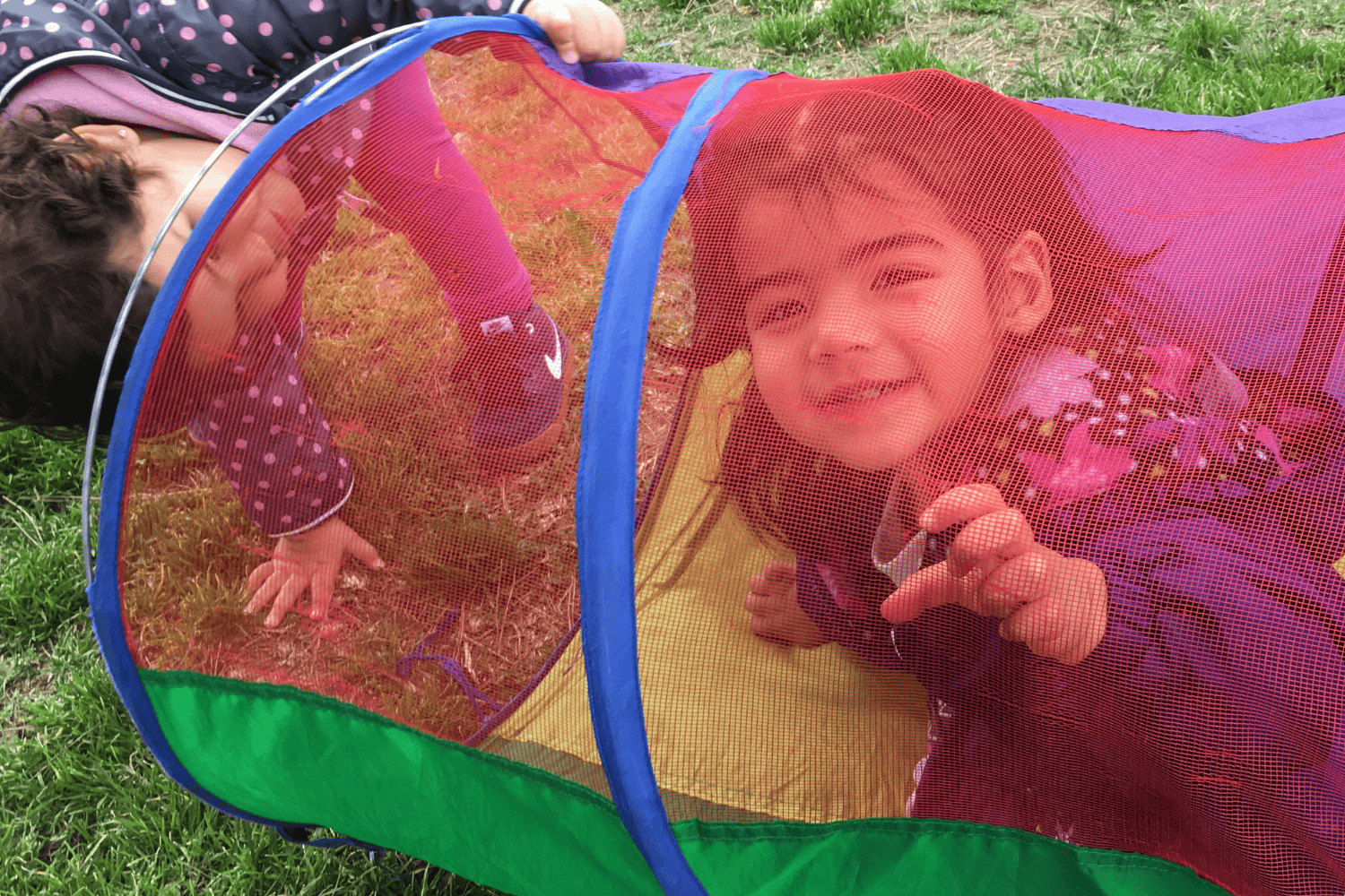 Toddler girls playing outside in colorful mesh tunnel