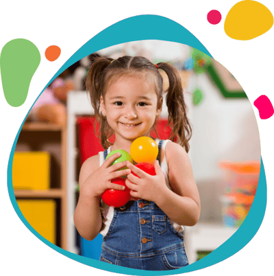 Preschool girl holding colorful balls in a classroom