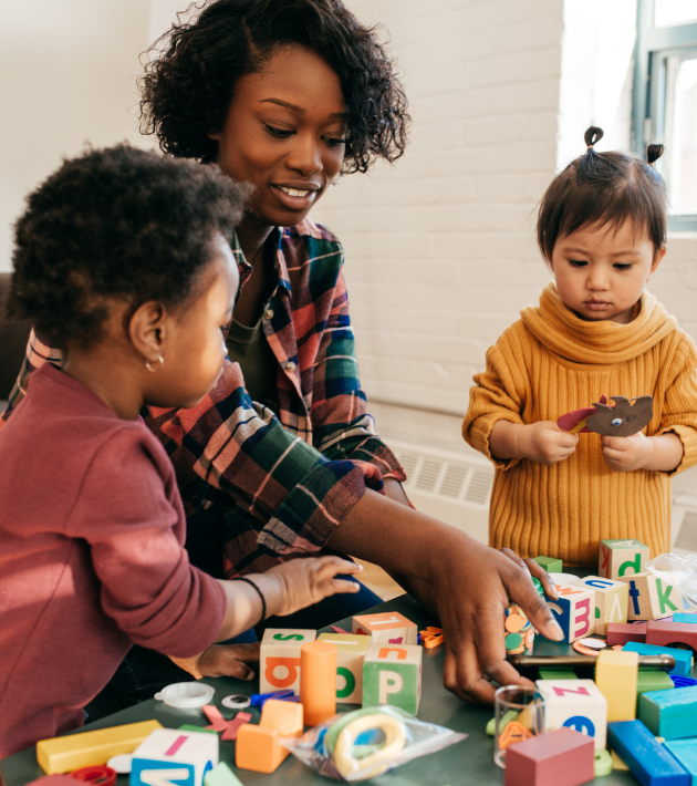 A daycare provider plays with blocks with two toddler girls