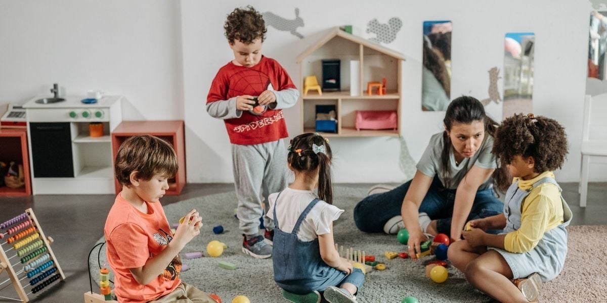 several preschool- age children and a teacher playing with blocks on the floor of a classroom